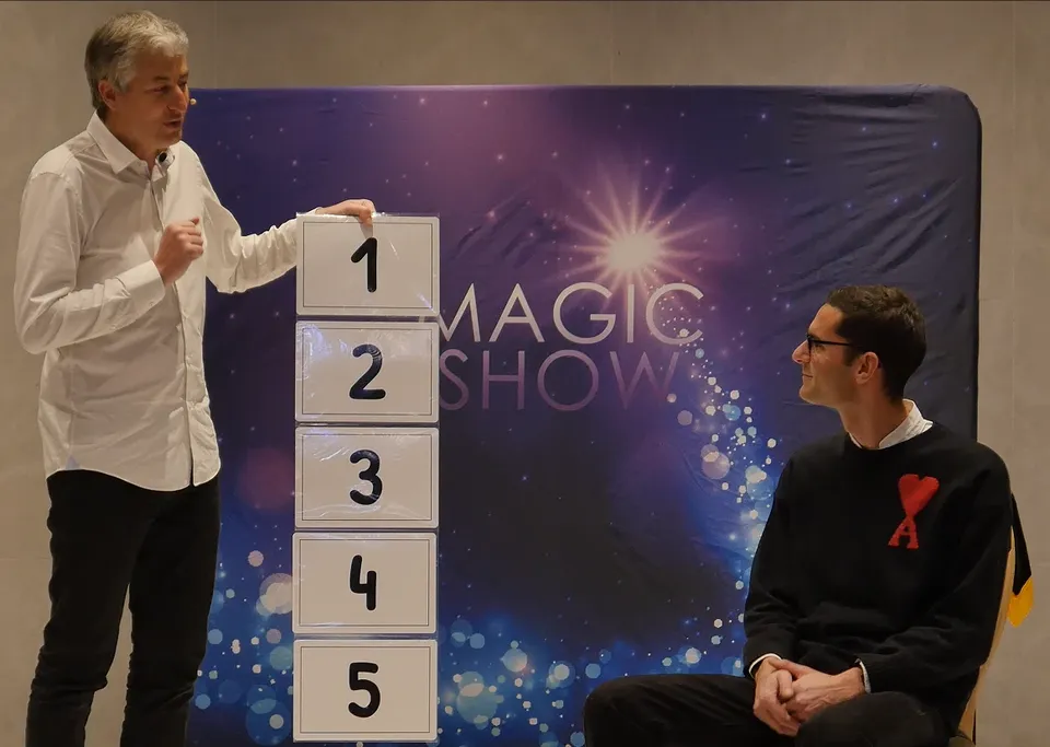 Ari, mentaliste, face à un spectateur volontaire pendant un spectacle de mentalisme avec cinq cartes numérotées de 1 à 5